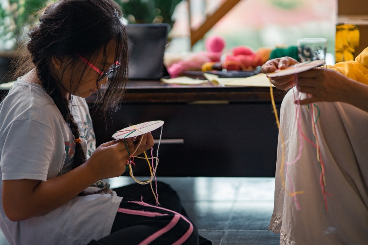 Young girl learning crafting with teacher, creating with colourful yarn